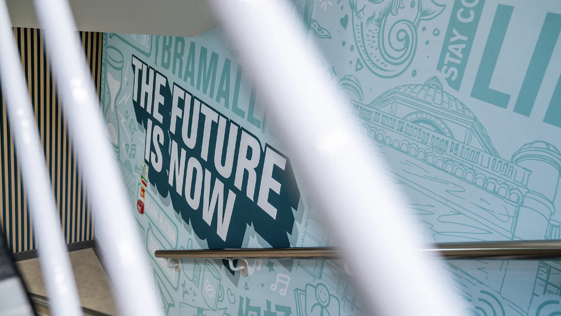 The 'The future is now' stairwell mural seen through the white balustrade, with the Barber Institute illustration alongside