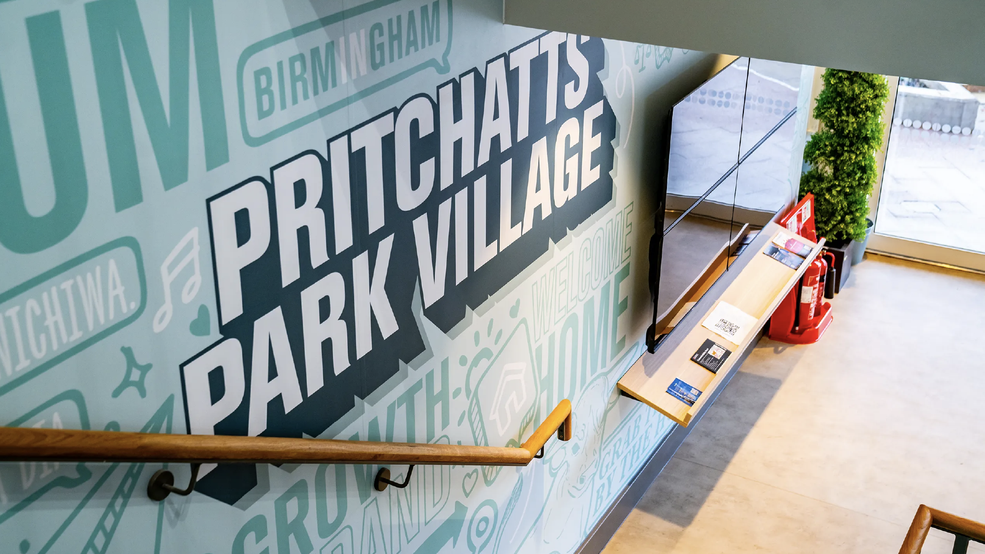 Installed stairwell graphic reading 'Pritchatts Park Village' in white type on a teal illustrated wall, with a timber handrail across it