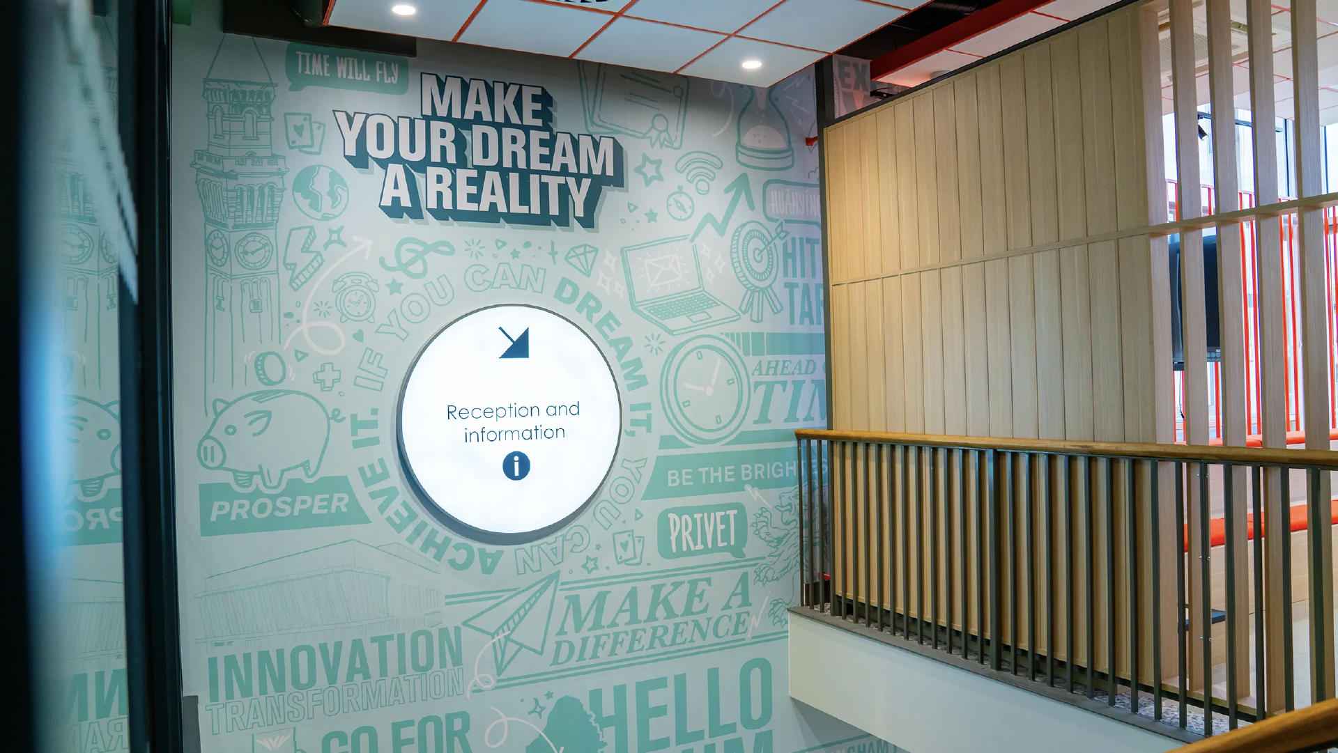 The 'Make your dream a reality' reception wall seen from the stair landing, with the circular information sign at its centre